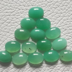 May include: A collection of sixteen oval-shaped, polished green gemstones arranged in a triangular pattern. The gemstones have a smooth, glossy surface and vary slightly in shade, with some showing minor inclusions.
