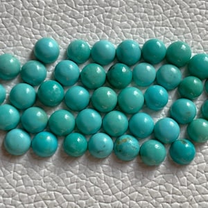 May include: A collection of 30 turquoise cabochons, each with a smooth, rounded surface. The stones are a vibrant blue-green color and are arranged in a loose cluster.