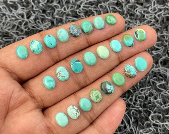 May include: A collection of oval-shaped turquoise cabochons in various shades of blue and green. The stones are arranged on a hand, showcasing their size and color variations.