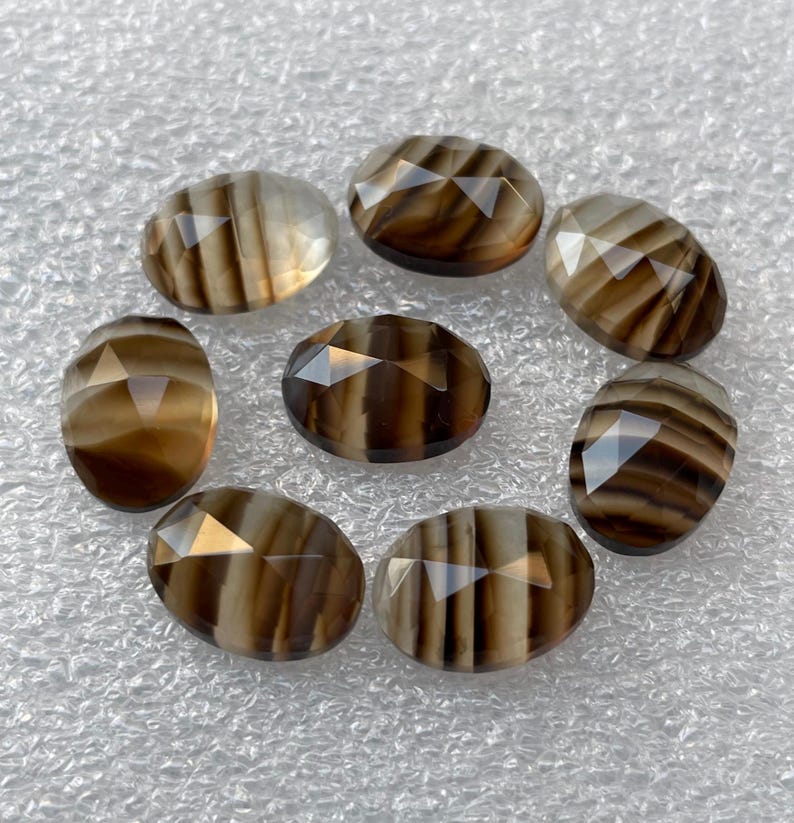 May include: Eight oval-shaped, faceted, brown and white agate gemstones. The gemstones have a striped pattern and are arranged in a circle.