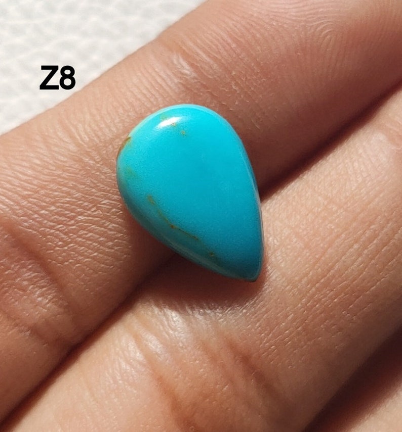May include: A teardrop-shaped turquoise cabochon with a blue-green color and brown veins. The stone is approximately 1 inch long.