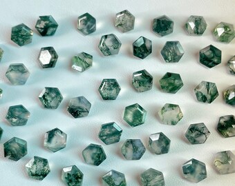 May include: A collection of green moss agate stones, each cut into a hexagonal shape. The stones have a variety of green and white patterns.