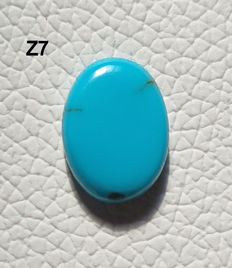 May include: A bright turquoise oval cabochon gemstone with dark brown veins. The stone is set against a white background. Z7.