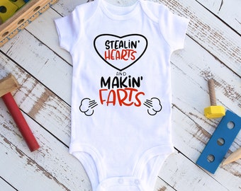 May include: White baby onesie with a red heart and black text that reads "Stealin' Hearts and Makin' Farts".
