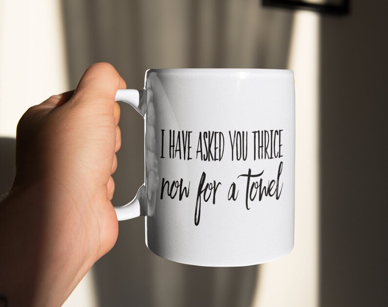 May include: White ceramic mug with black text that reads "I have asked you thrice now for a towel".