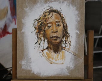 May include: An oil painting on canvas of a person with curly brown hair and a neutral expression. The portrait is set against a white background with a brown canvas border. The artwork is displayed on a wooden easel.