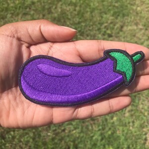 May include: A purple and green embroidered eggplant patch. The eggplant is outlined in black and has a green stem.