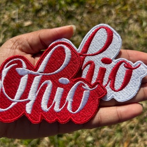 May include: Two embroidered patches featuring the word "Ohio" in a cursive font. One patch is red with white lettering, and the other is white with red lettering.
