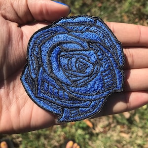 May include: A blue embroidered rose patch with black stitching. The rose is in full bloom and has a detailed design.