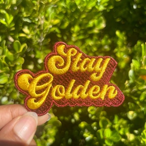 May include: A red and gold embroidered patch with the text "Stay Golden" in a retro font.