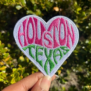 May include: White heart-shaped patch with the words "HOUSTON TEXAS" embroidered in pink and green.
