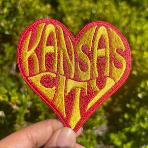 Peut inclure: Un patch en forme de cœur rouge avec les mots "Kansas City" brodés en or.