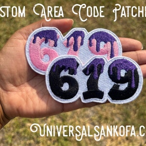 May include: Three iron-on patches with dripping purple paint and black numbers 6, 7, and 9. The patches are on a white background and are held in a hand.