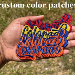 May include: A set of four embroidered patches in red, yellow, orange, and blue. Each patch features the word "Colorado" in a stylized font.
