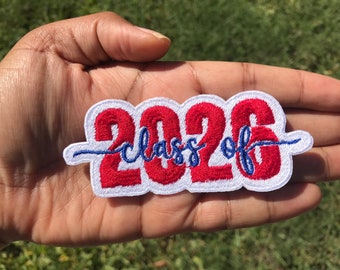 Op de afbeelding: Gestikt rood en blauw patch met de tekst "Class of 2026" op een witte achtergrond.