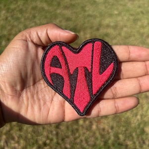 May include: A red heart-shaped patch with the letters ATL in black outlined in white.