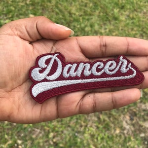 May include: An iron-on patch embroidered in red and white with the word "Dancers" in a white cursive font.