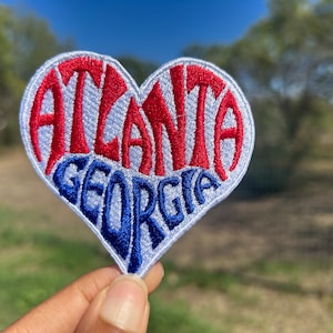 May include: A white heart-shaped patch with the words "Atlanta Georgia" embroidered in red and blue thread.