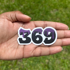 May include: A die-cut sticker featuring the numbers 369 in a bold, black font. The top portion of each number has a purple liquid drip effect, and the entire design is outlined with a thick white border for a clean, high-contrast appearance.