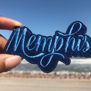 May include: A blue embroidered patch with the word "Memphis" in a stylized font.