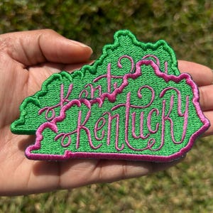 May include: Green felt outline of the state of Kentucky with the words "I love Kentucky" embroidered in pink.