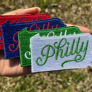 May include: Four embroidered patches in the shape of the state of Pennsylvania, with the word "Philly" written in a cursive font. The patches are red, blue, green, and white.