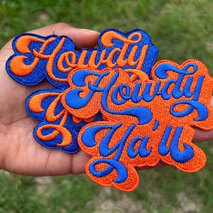 May include: A set of three embroidered iron-on patches with the phrase "Howdy Ya'll" in a blue and orange color scheme.