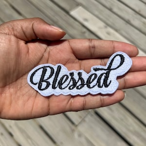May include: White fabric patch with black embroidered lettering that reads "Blessed".