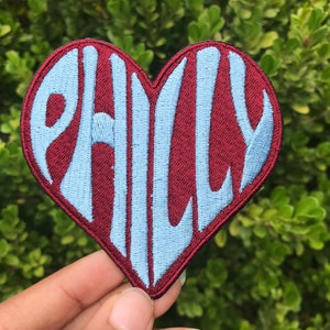 May include: A red heart-shaped patch with the word "PHILLY" embroidered in white.