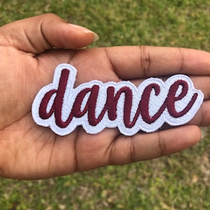 May include: A white iron-on patch with the word "dance" embroidered in maroon.