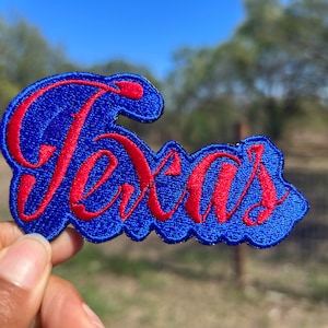 May include: A blue and red embroidered patch with the word "Texas" in a cursive font.
