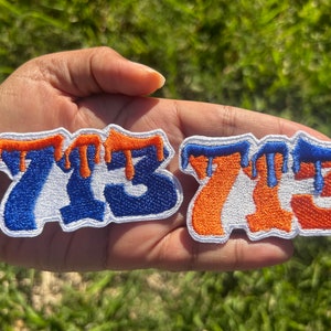 May include: Two embroidered iron-on patches with the numbers "713" in a dripping style. The patches are white with blue and orange embroidery. The left patch has blue dripping paint and the right patch has orange dripping paint.