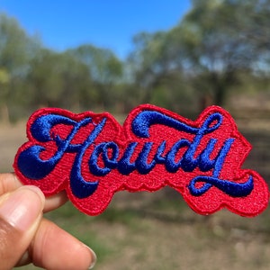 May include: Red and blue embroidered patch with the word "Howdy" in a stylized font.
