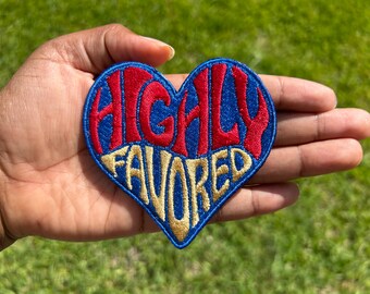 May include: A blue heart-shaped embroidered patch with the words "HIGHLY FAVORED" in red and gold lettering.