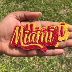 May include: A set of four embroidered iron-on patches with the word "Miami" in yellow lettering on a red background.