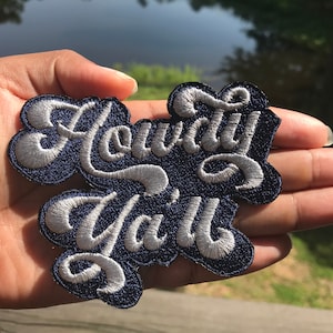 May include: A blue and white embroidered patch with the text "Howdy Ya'll" in a cursive font.