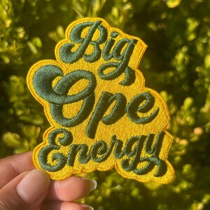 May include: A yellow and green embroidered patch with the text "Big Ope Energy" in a retro font.