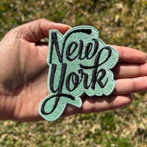 May include: A green embroidered patch with black lettering that reads "New York".