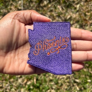 May include: Purple felt patch in the shape of the state of Arizona with the word "Phoenix" embroidered in orange thread.