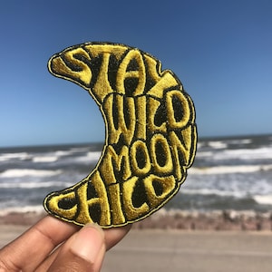 May include: A yellow crescent moon shaped patch with the text "Stay Wild Moon Child" embroidered in black.