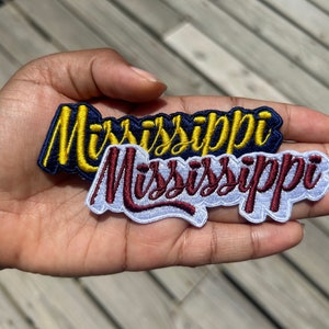May include: Two embroidered patches with the word "Mississippi" in different styles. The top patch is navy blue with yellow lettering. The bottom patch is white with burgundy lettering.