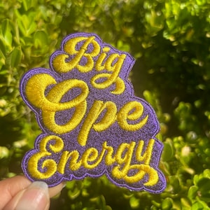 May include: A purple embroidered patch with the text "Big Ope Energy" in yellow thread.