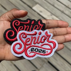 May include: Two embroidered patches with the word "Senior" in red lettering. One patch is black with white lettering and the other is white with black lettering. The white patch has the year "2025" in black lettering.