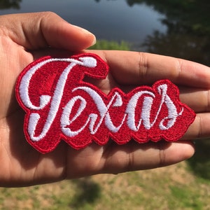 May include: Red embroidered patch with white lettering that says "Texas".
