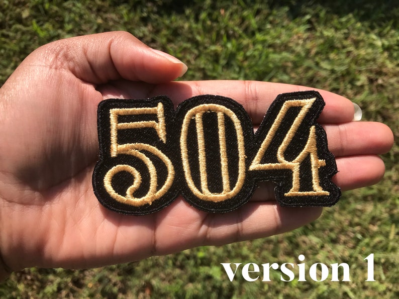 May include: A black embroidered patch with the numbers "504" in gold thread. The patch is held in a hand.