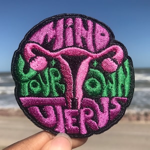 May include: A pink and green embroidered patch with the text "MIND YOUR OWN UTERUS" and a stylized image of a uterus.
