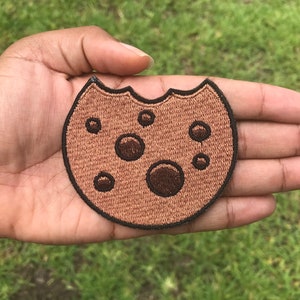 May include: A brown and black embroidered cookie patch with chocolate chips.