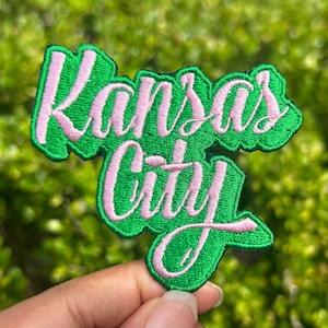 May include: Green and pink embroidered patch with the text "Kansas City" in a stylized font.