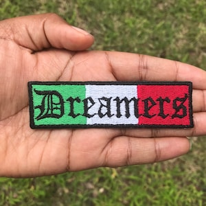 May include: A green, white, and red embroidered patch with the word "Dreamers" in black lettering.