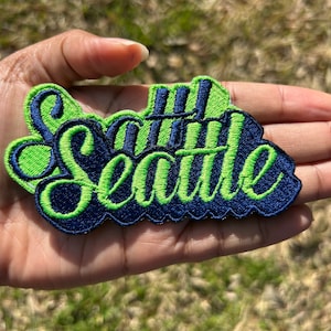 May include: Green and blue embroidered patch with the word "Seattle" in a stylized font.